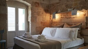 Una habitación con paredes de piedra, una cama, una silla y un ventanal.