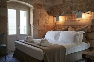 A stone-walled room with a bed, a chair, and a window.