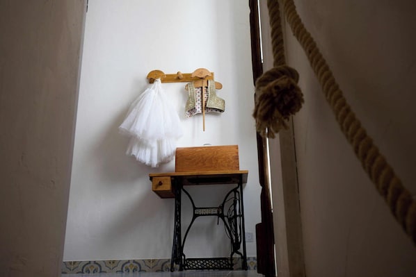 Une pièce avec une table en bois, une machine à coudre Singer et un porte-vêtements mural sur lequel sont suspendus un vêtement blanc et un gilet à motifs.