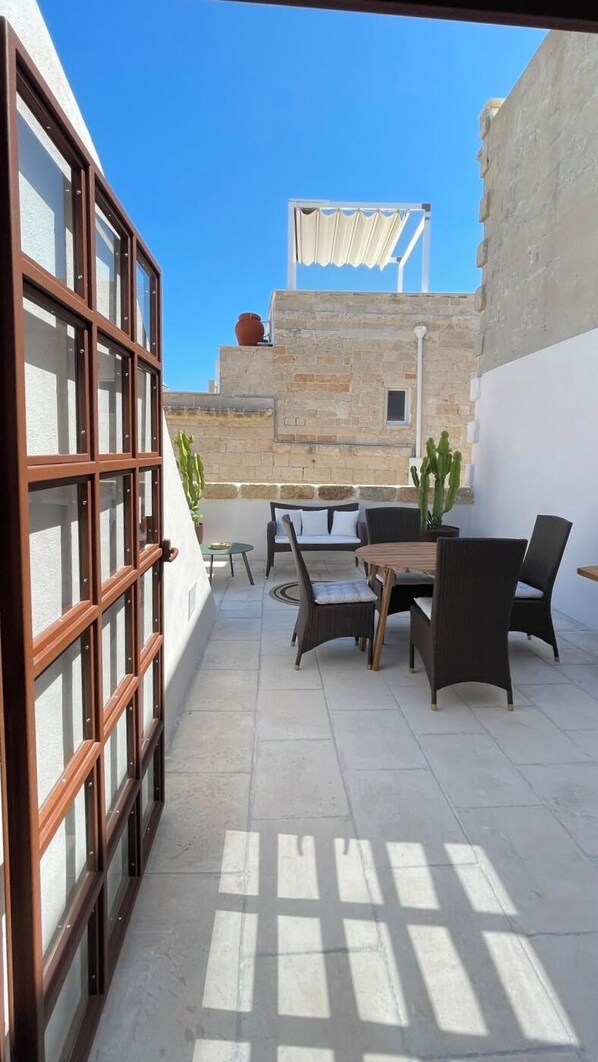 Un patio al aire libre con una mesa y sillas, una planta en maceta y vista a un edificio con fachada de piedra.