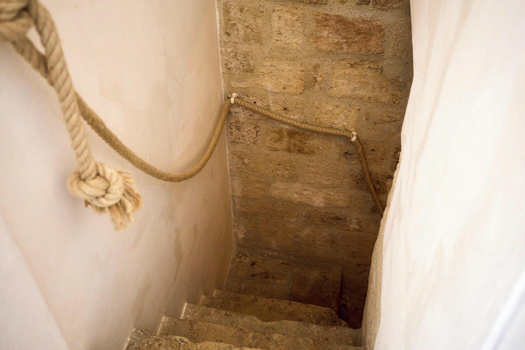 A narrow staircase with a rope handrail and a decorative knot at the top.