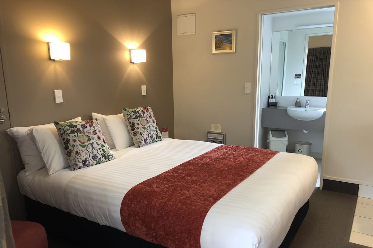 Habitación de hotel con una cama grande, dos lámparas de pared, un cuadro, un lavamanos y un espejo en el baño.