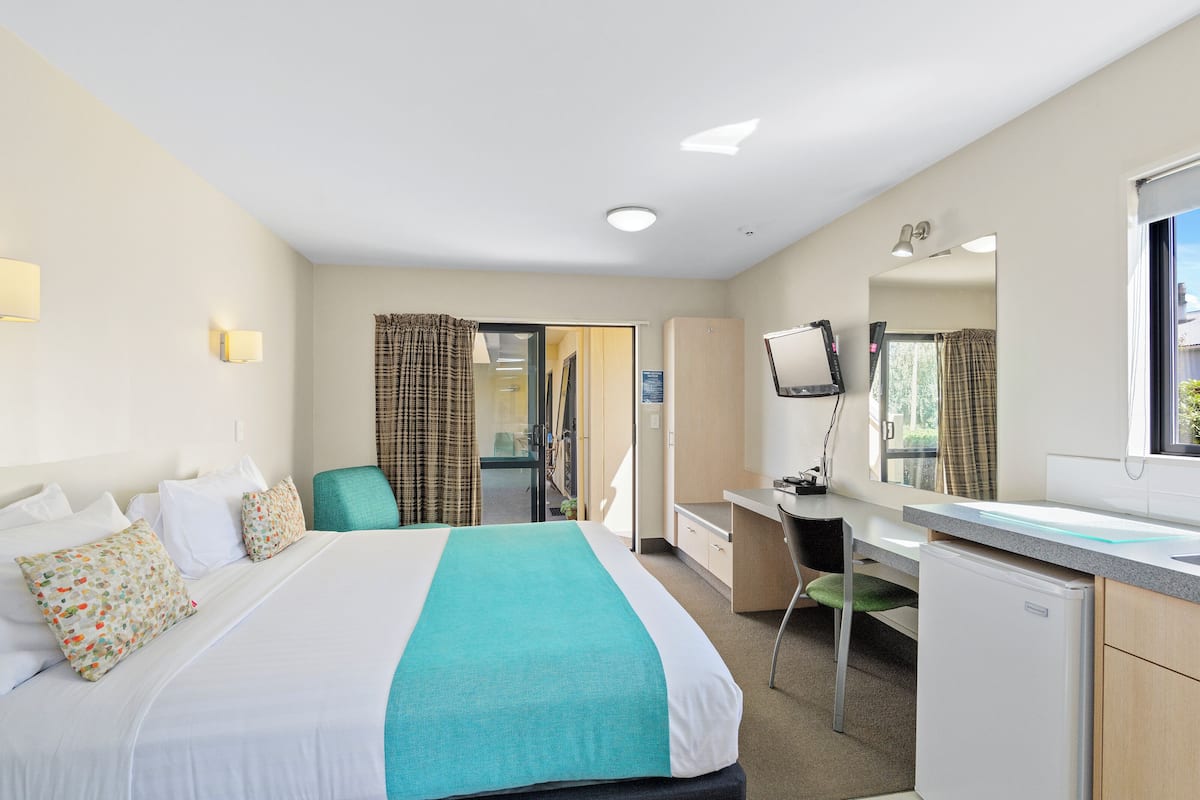 Una habitación de hotel con cama, escritorio, silla, televisor y espejo.