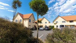A residential building with a parking area, surrounded by greenery and a clear sky.