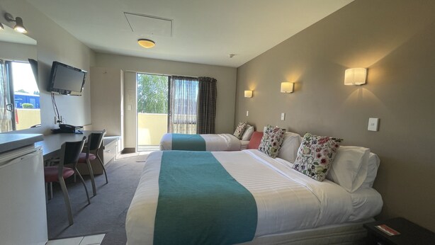 A hotel room with two beds, a desk, a chair, a television, and a window with curtains.