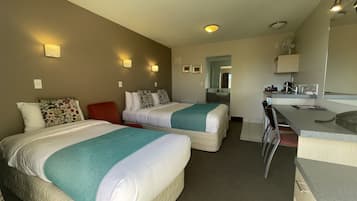 Habitación de hotel con dos camas, un escritorio, una silla, un espejo y un baño visible a través de una puerta abierta.
