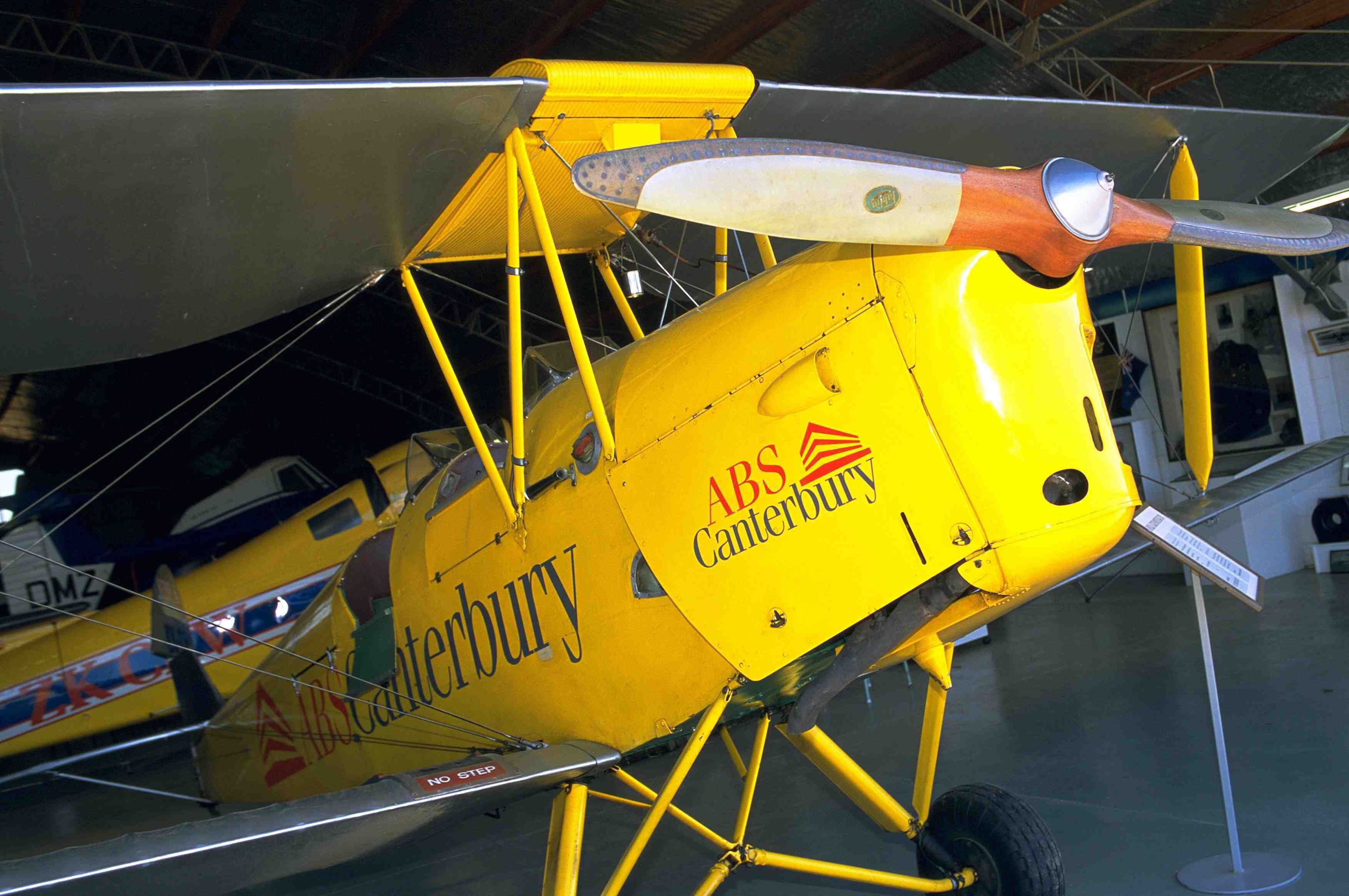 Un biplan jaune portant l’inscription « ABS Canterbury » est exposé dans un hangar.