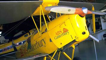 Un biplan jaune portant l’inscription « ABS Canterbury » est exposé dans un hangar.