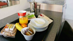 A breakfast tray with bread, fruit, and a beverage in a hotel room.