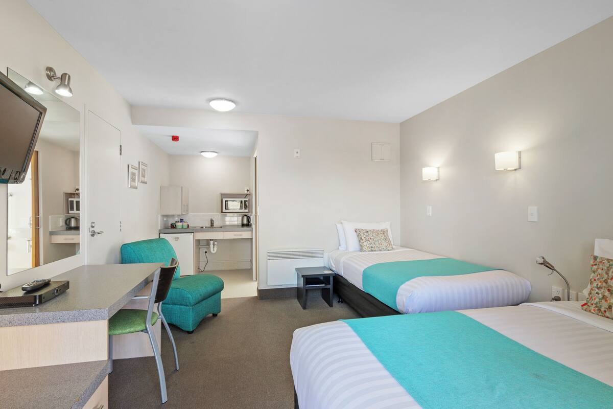 Habitación de hotel con dos camas, un escritorio, una silla, kitchenette y baño.