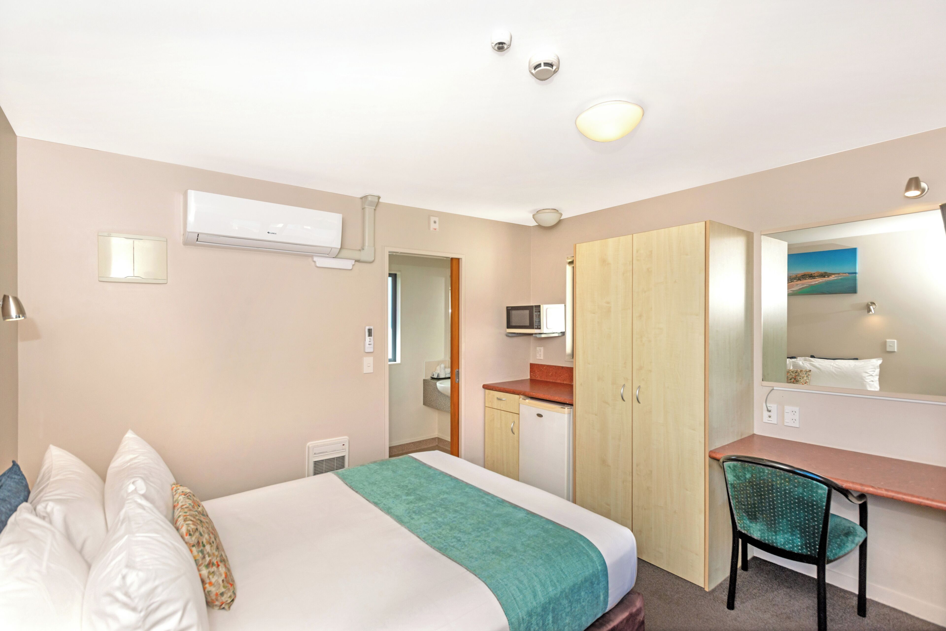 A hotel room with a bed, a desk, a chair, a microwave, and a small kitchenette.
