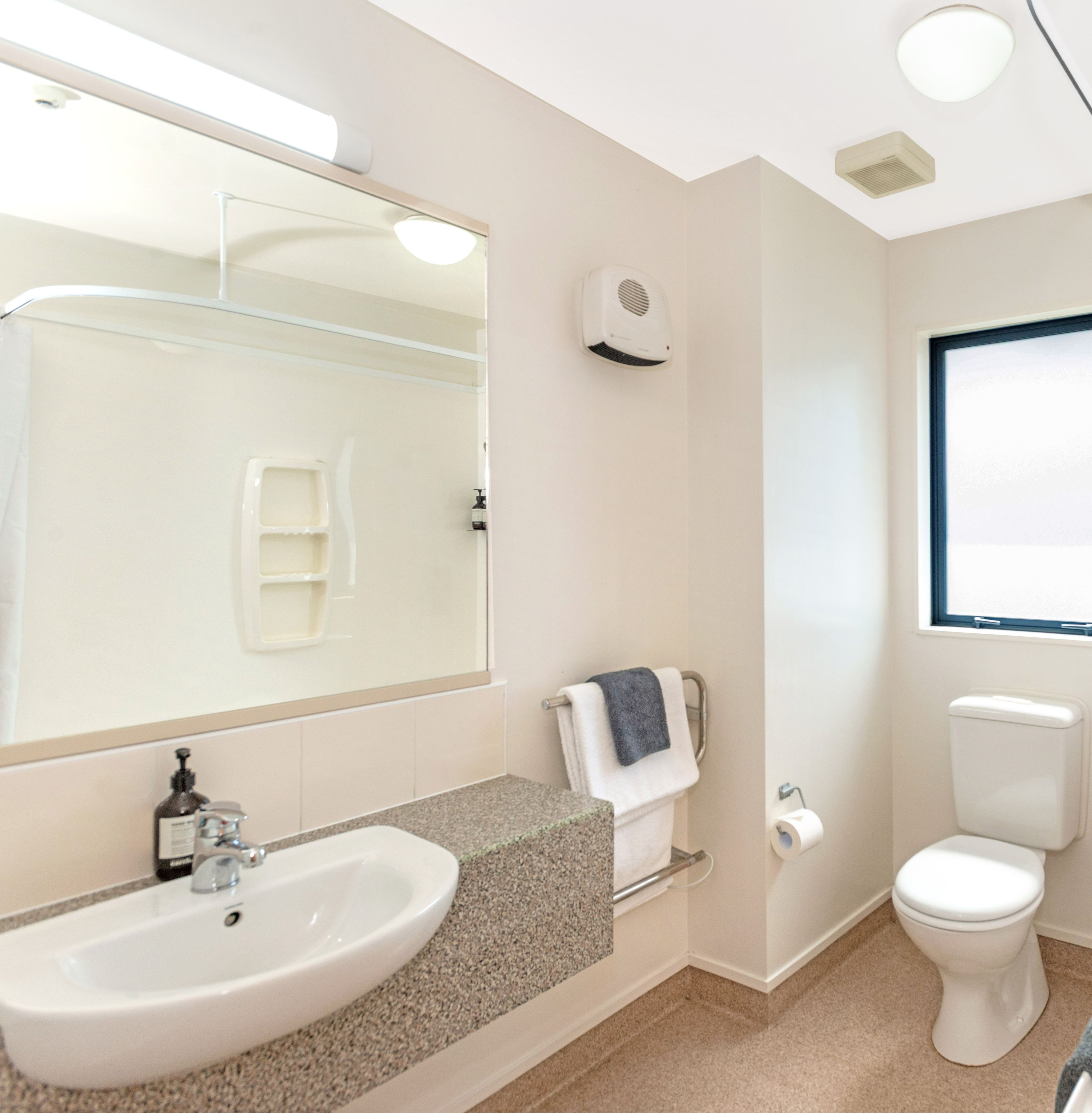 A bathroom with a sink, mirror, towel rack, toilet, and a window.