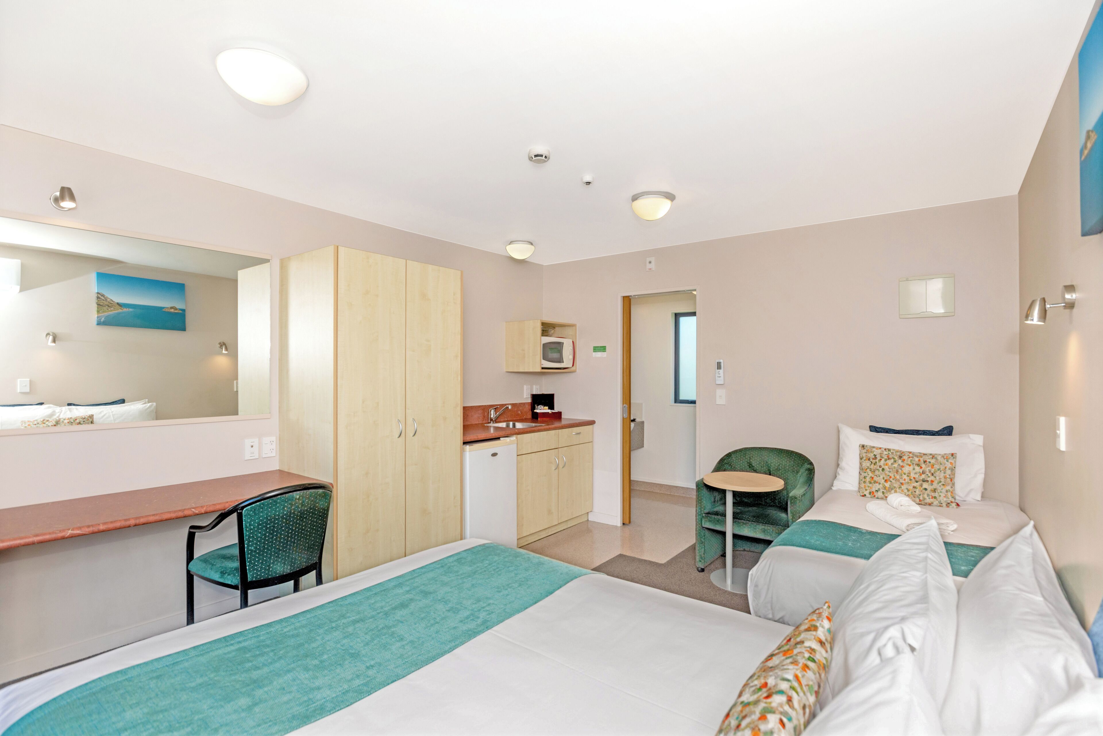 Habitación de hotel con cama, escritorio, silla, mesita y kitchenette.