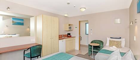 Habitación de hotel con cama, escritorio, silla, mesita y kitchenette.