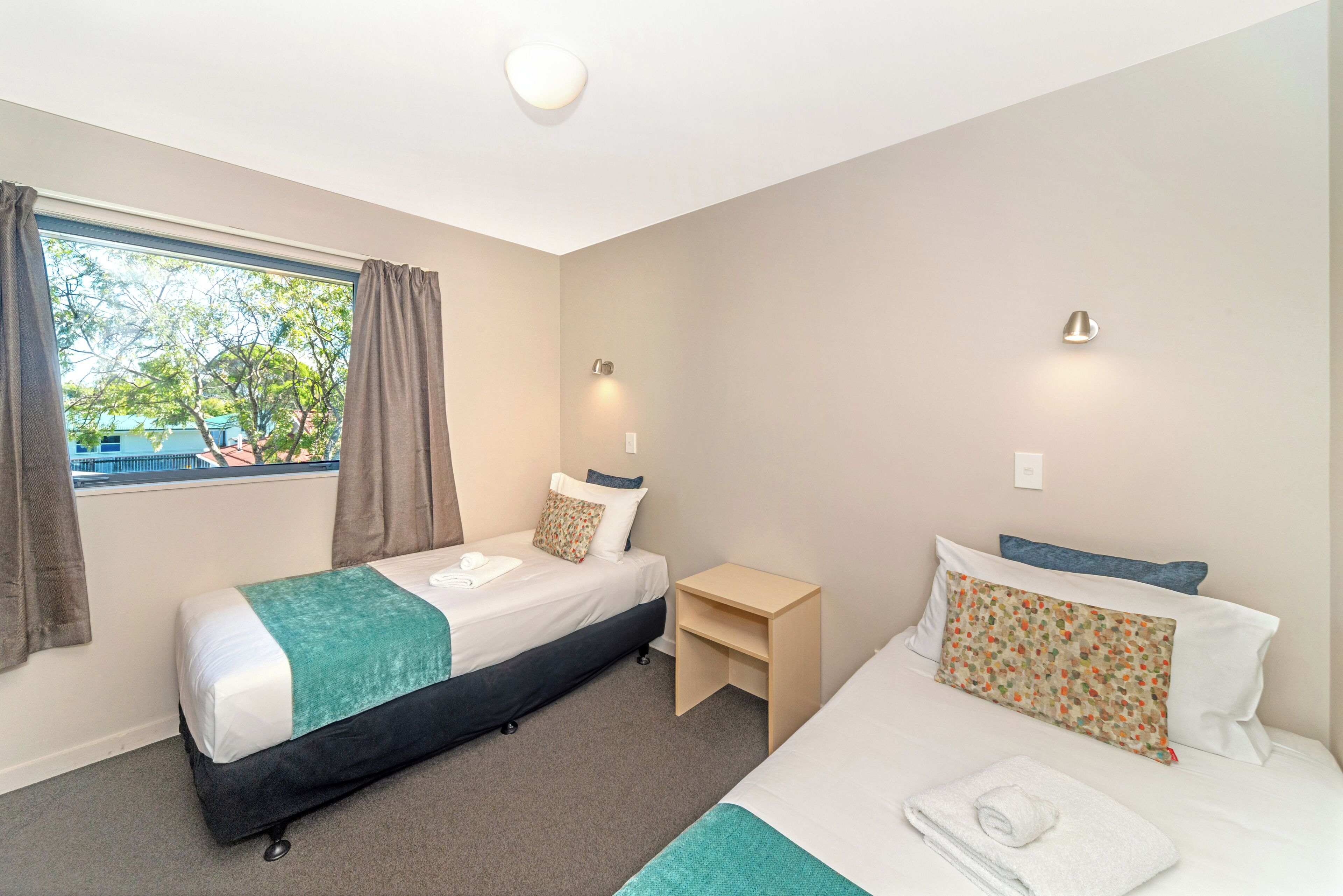 A hotel room with two beds, a small table, and a window with curtains.