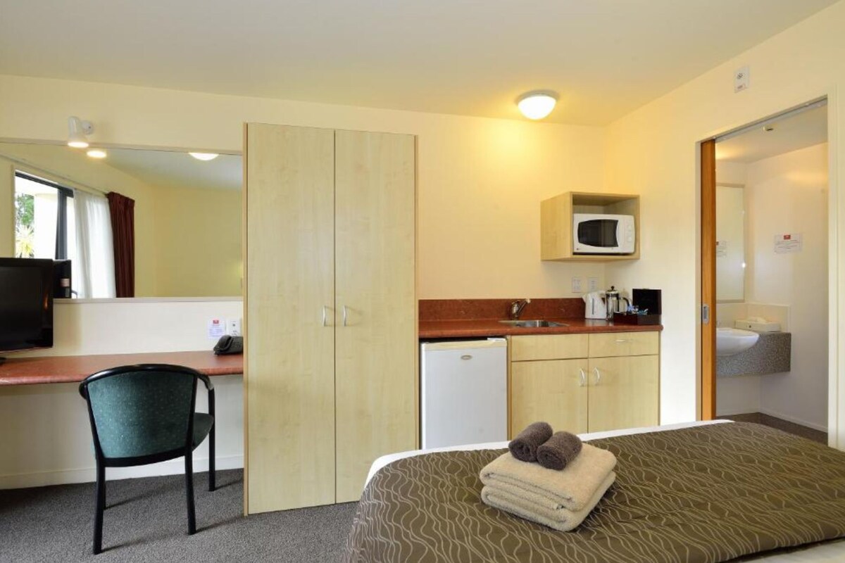 A room with a bed, a desk, a chair, a microwave, and a small kitchenette.