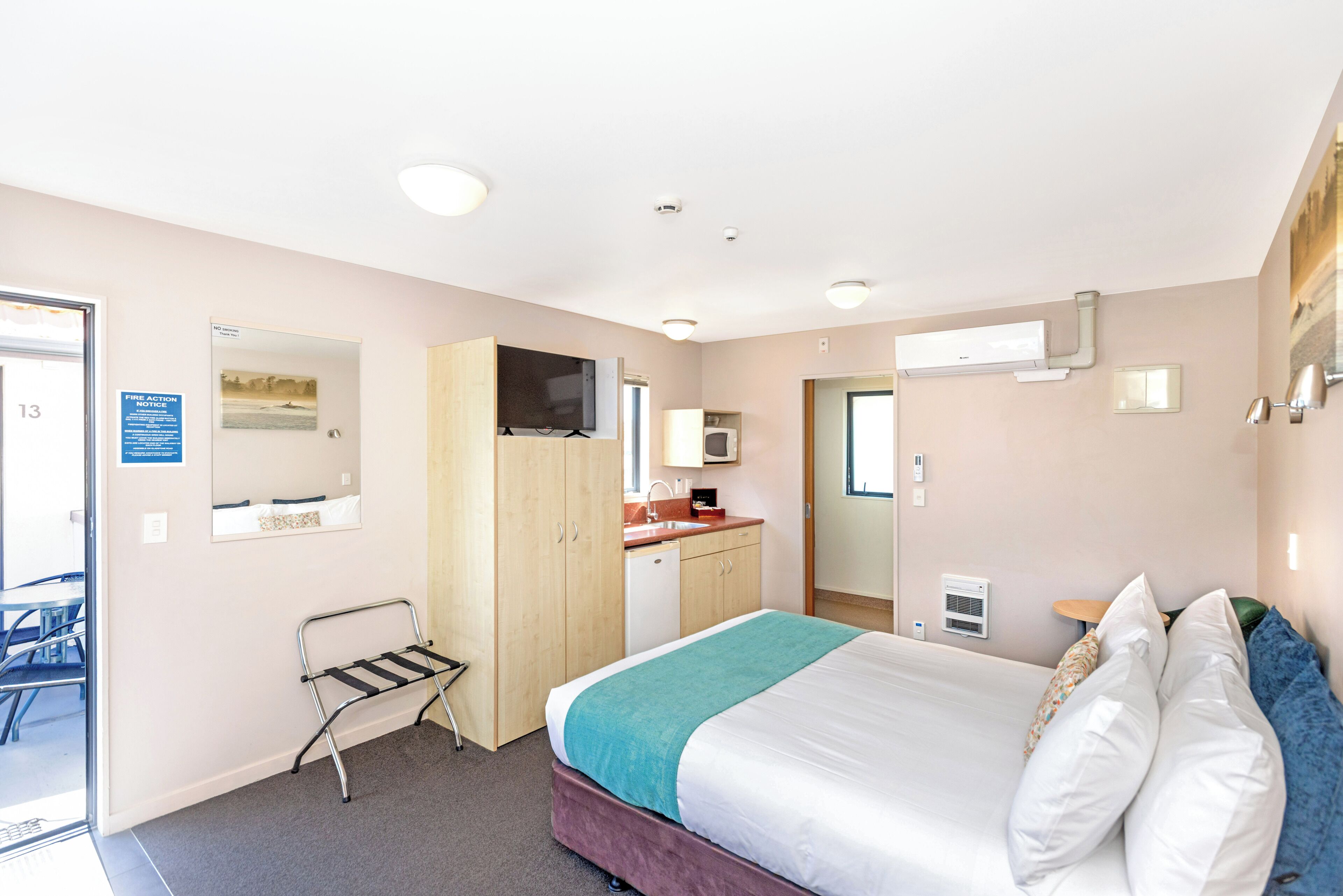 A hotel room with a bed, a desk, a chair, a mirror, a TV, a sink, and a wardrobe.
