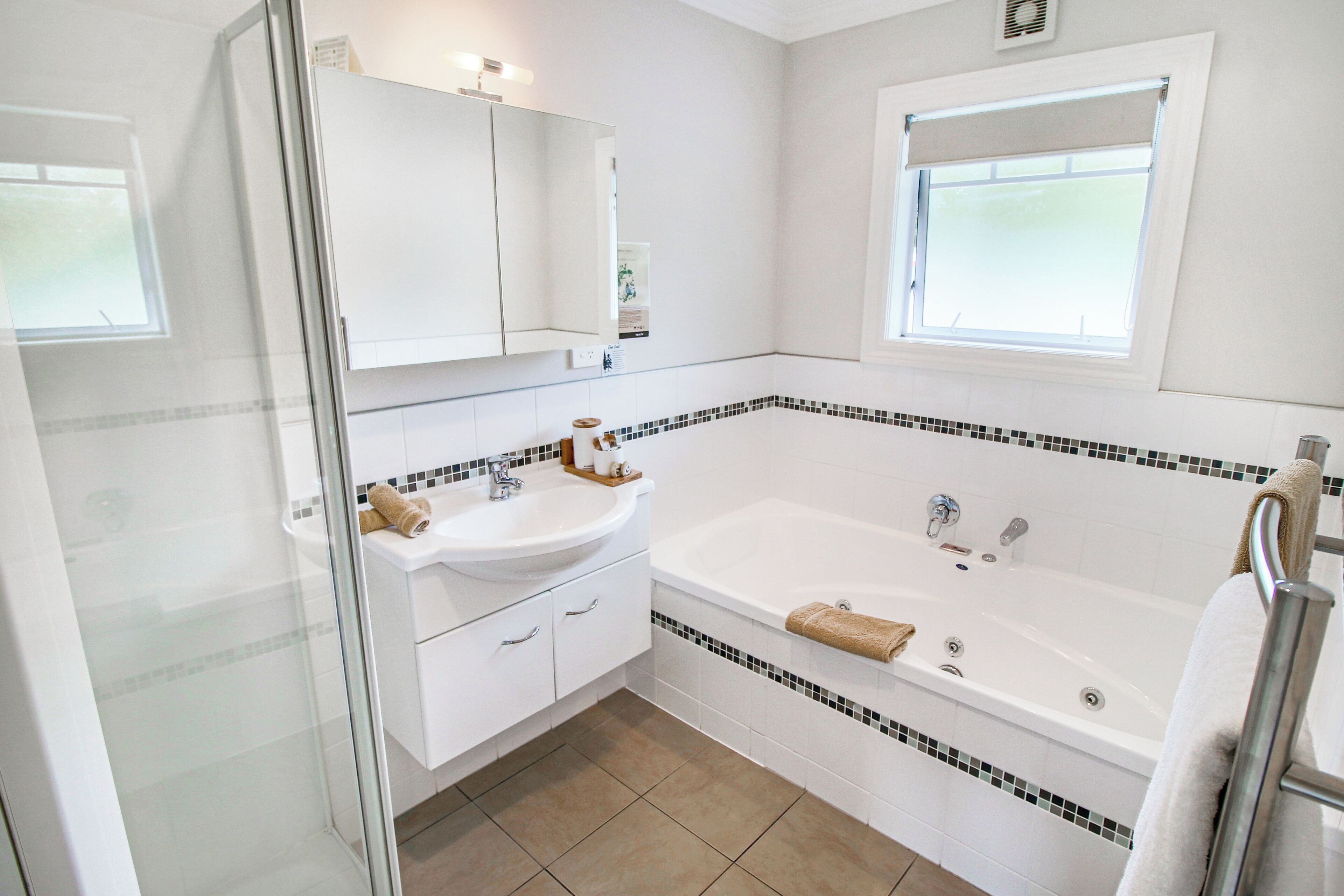 A modern bathroom with a white sink, vanity, and bathtub. There is a window with a view of the sky, and a shower area with a glass door.