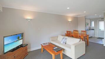 A living room with a television, sofa, coffee table, and dining area with chairs and a table.