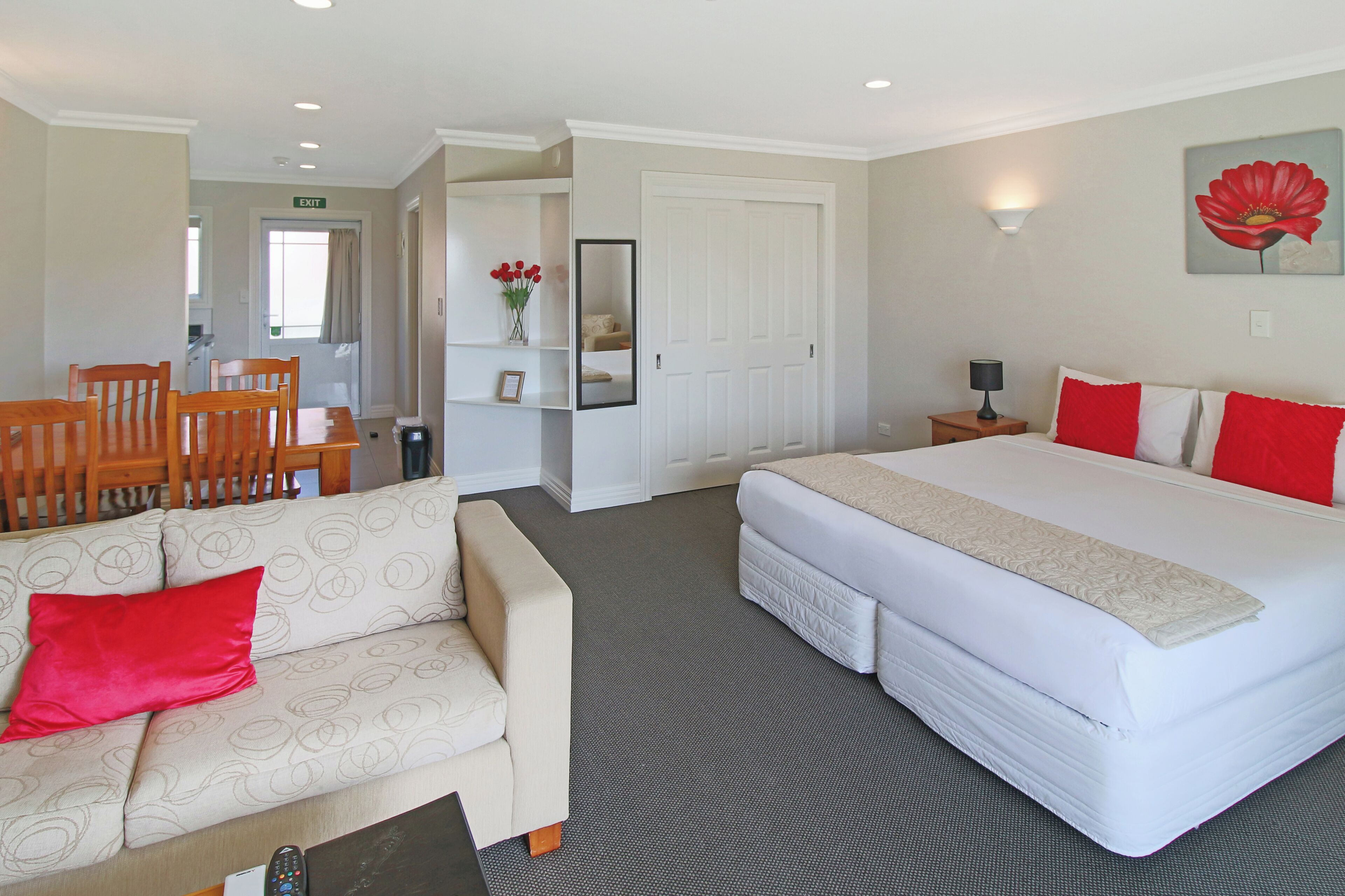 A hotel room with a bed, a sofa, a dining table with chairs, a small table with a lamp, and a painting on the wall.