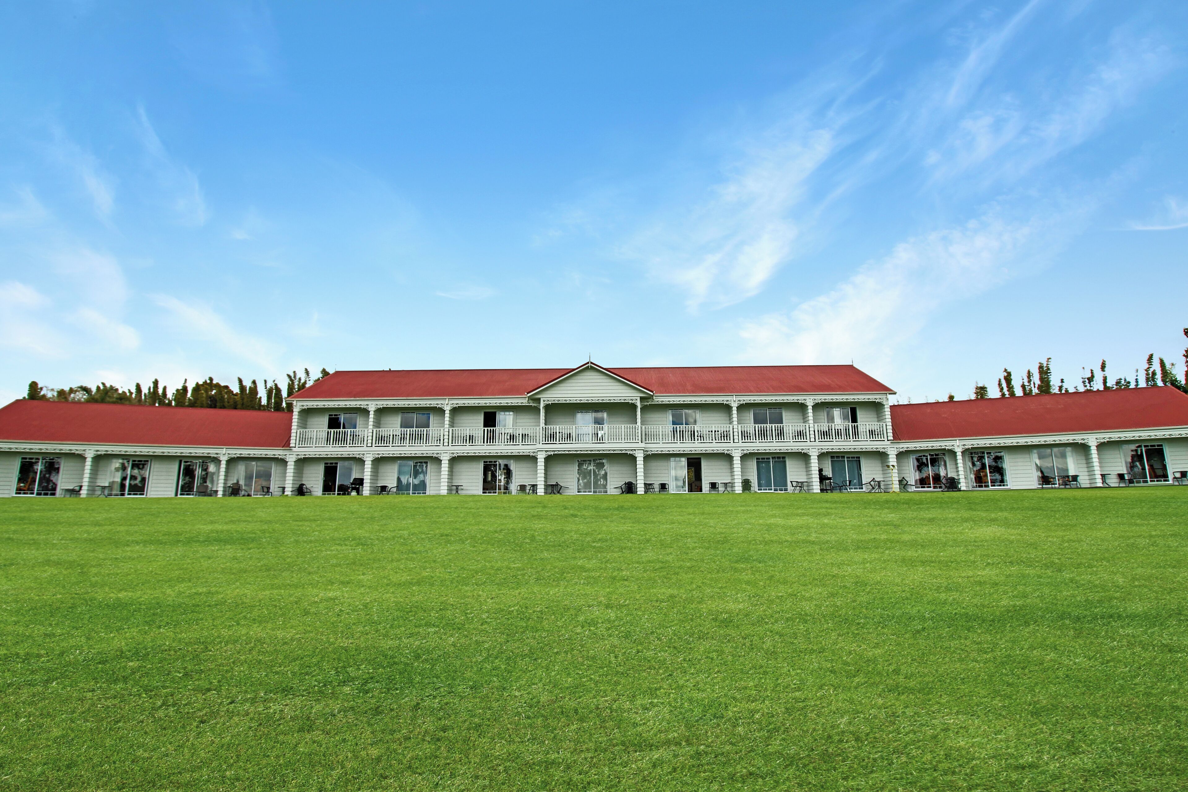 A large, white building with a red roof, multiple balconies, and a spacious lawn in front.
