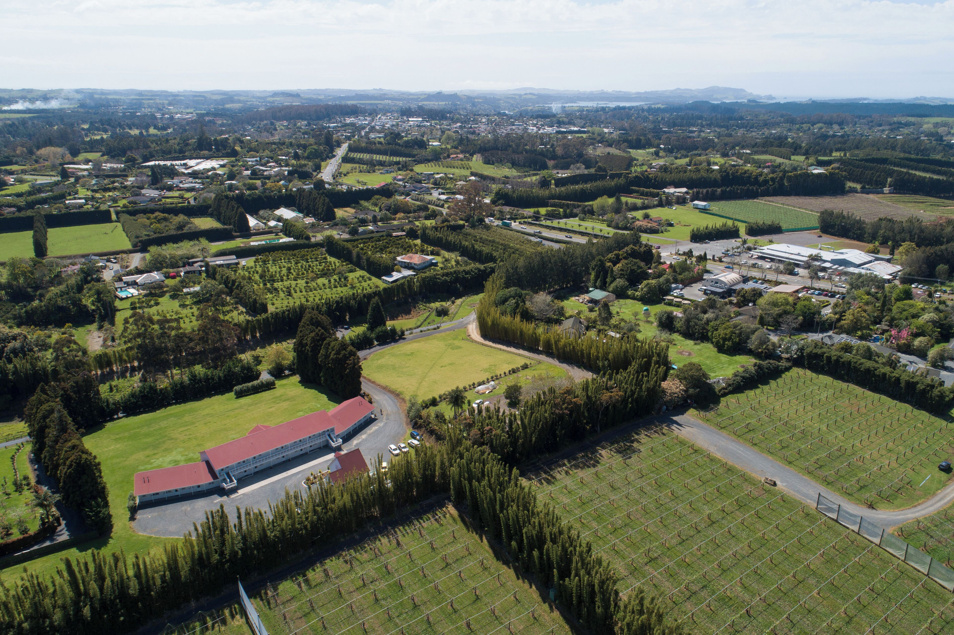 An aerial view of a rural area with fields, a large building with a red roof, and a road curving through the landscape.