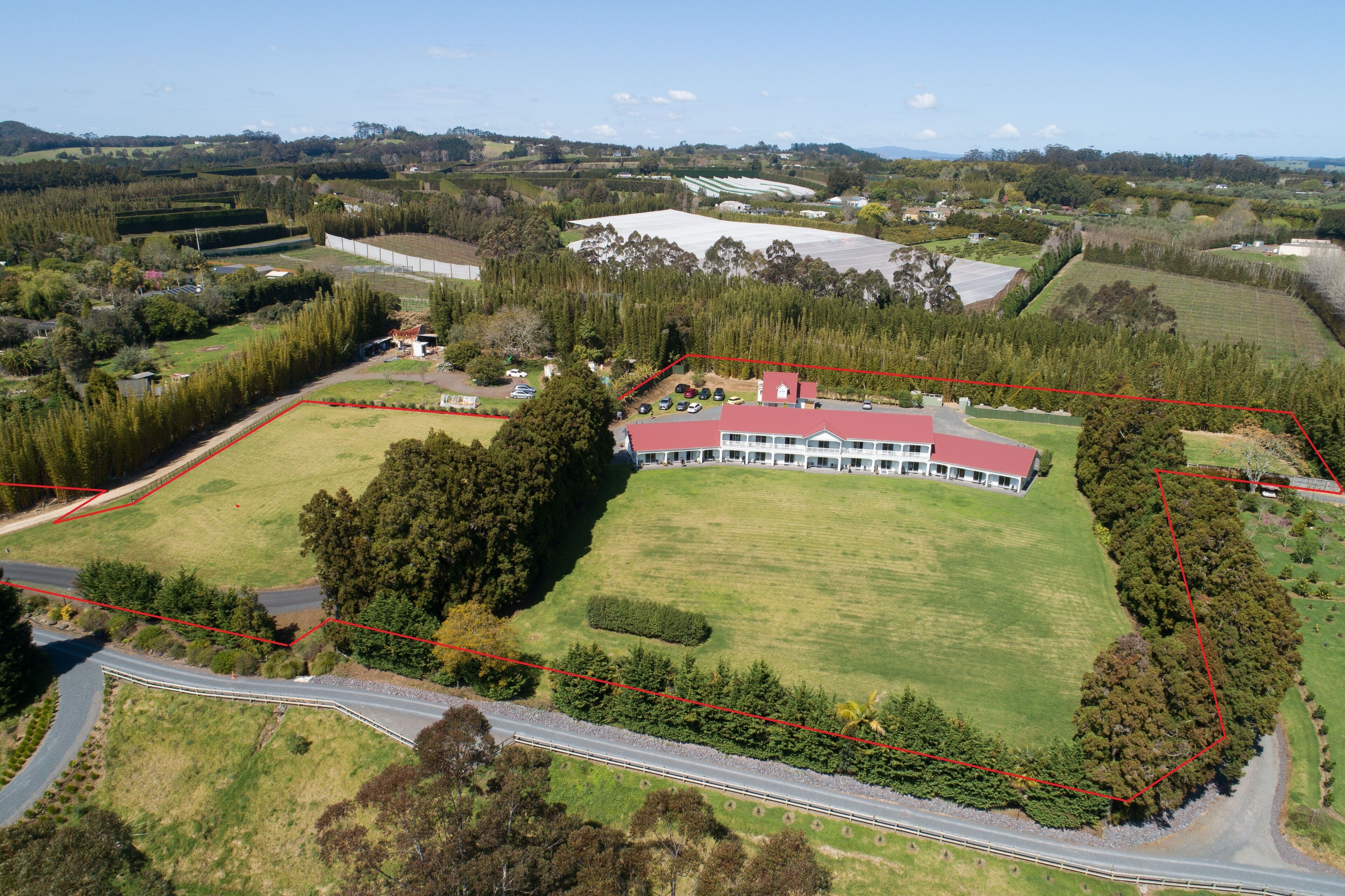 An aerial view of a property with a large building, a fenced area, and surrounding greenery.