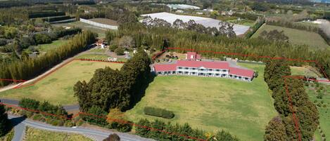 An aerial view of a property with a large building, a fenced area, and surrounding greenery.