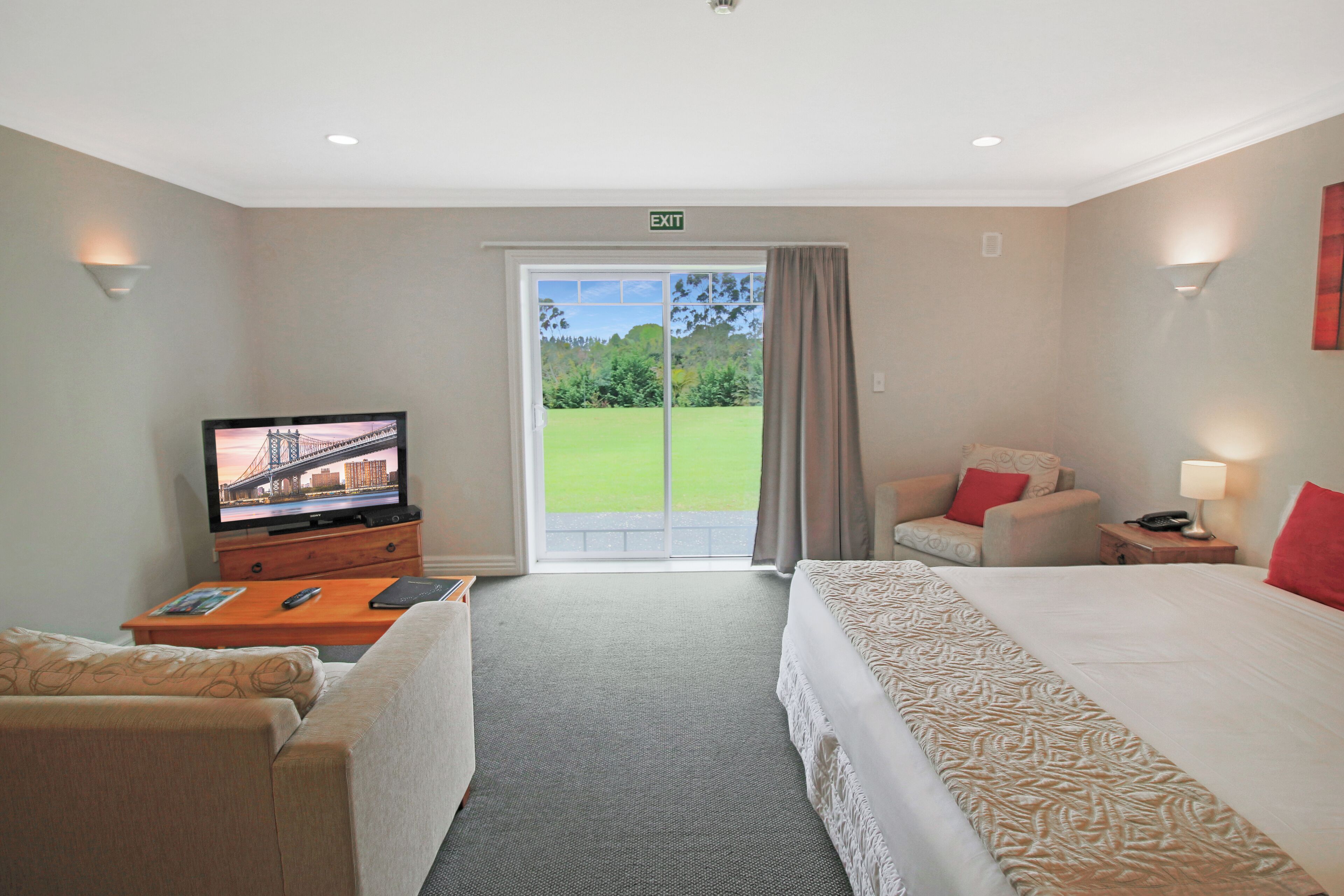 A hotel room with a bed, a TV, a sofa, a desk, and a view of a green landscape through a sliding door.