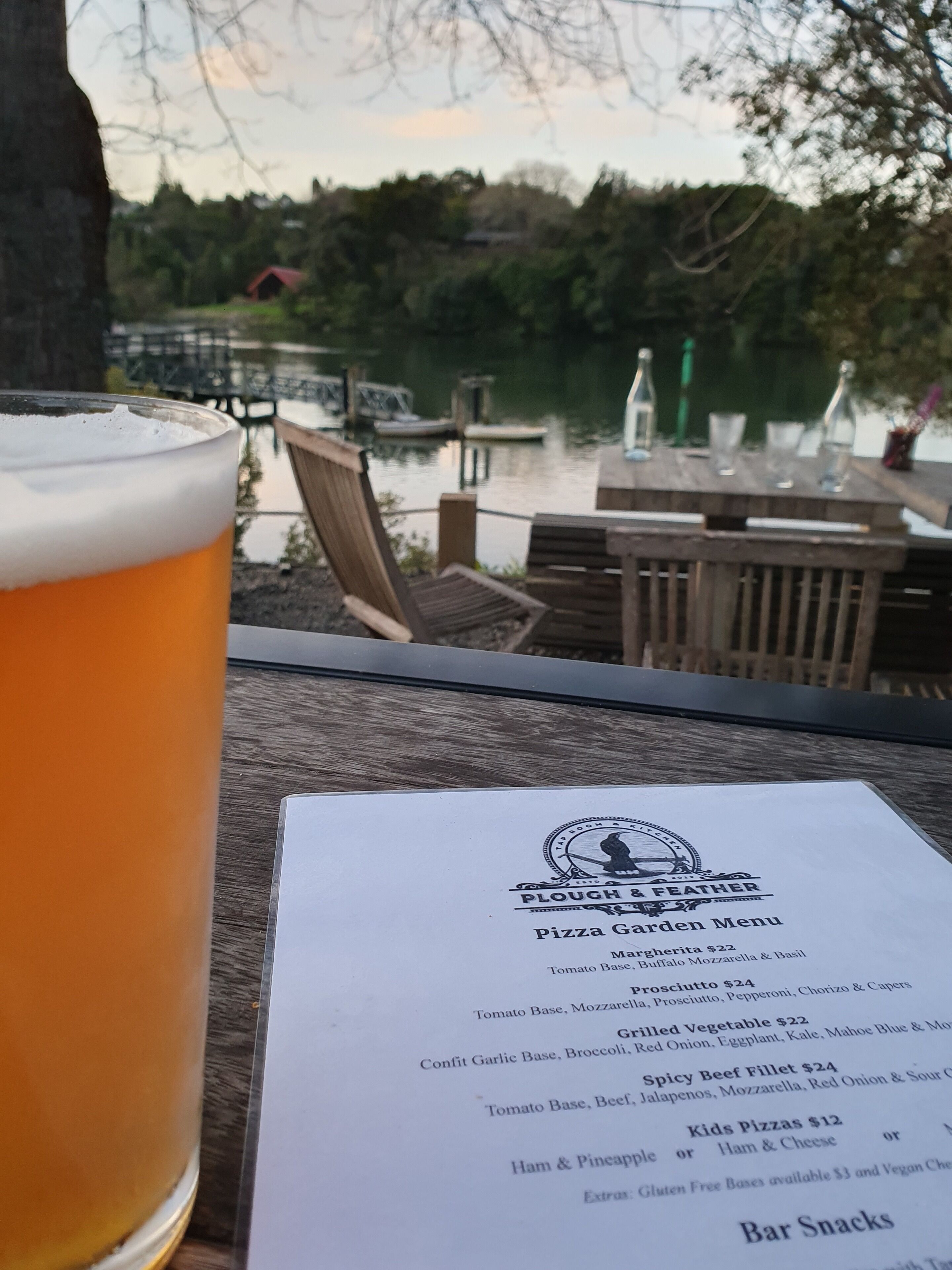A menu at a lakeside restaurant with a glass of beer in the foreground.