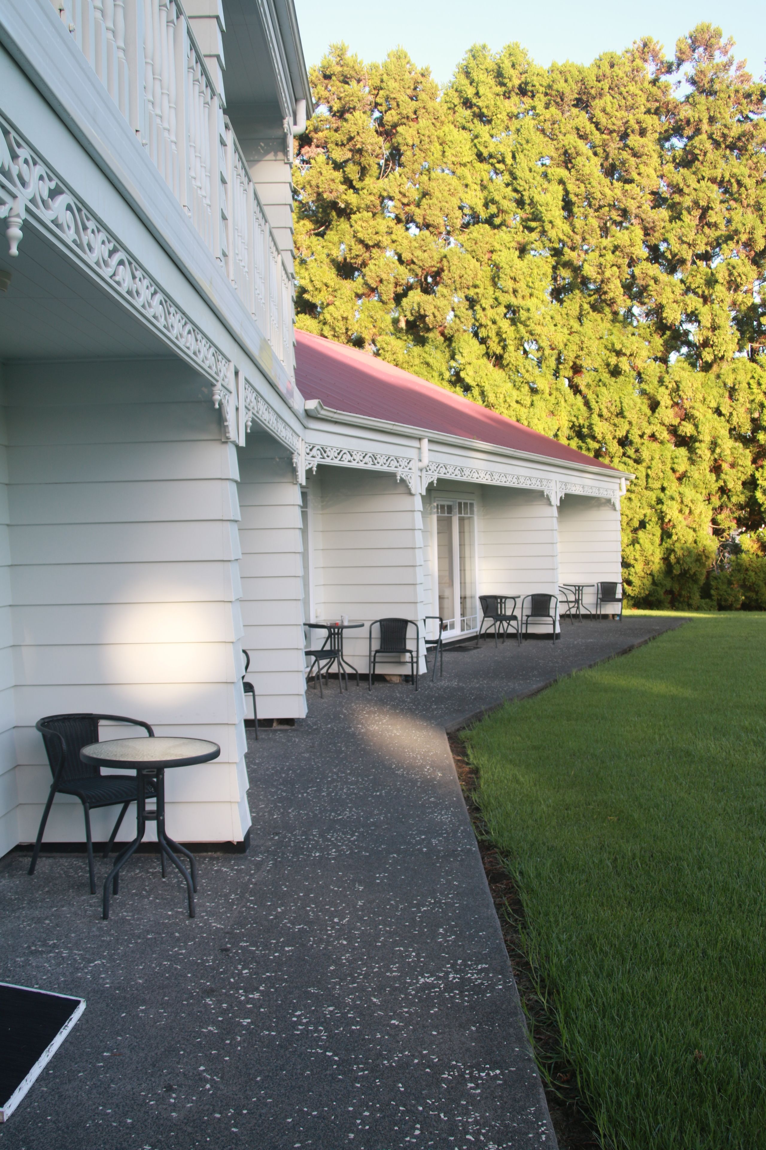 A building with a red roof and white walls, outdoor seating with chairs and tables, and a grassy area in front.