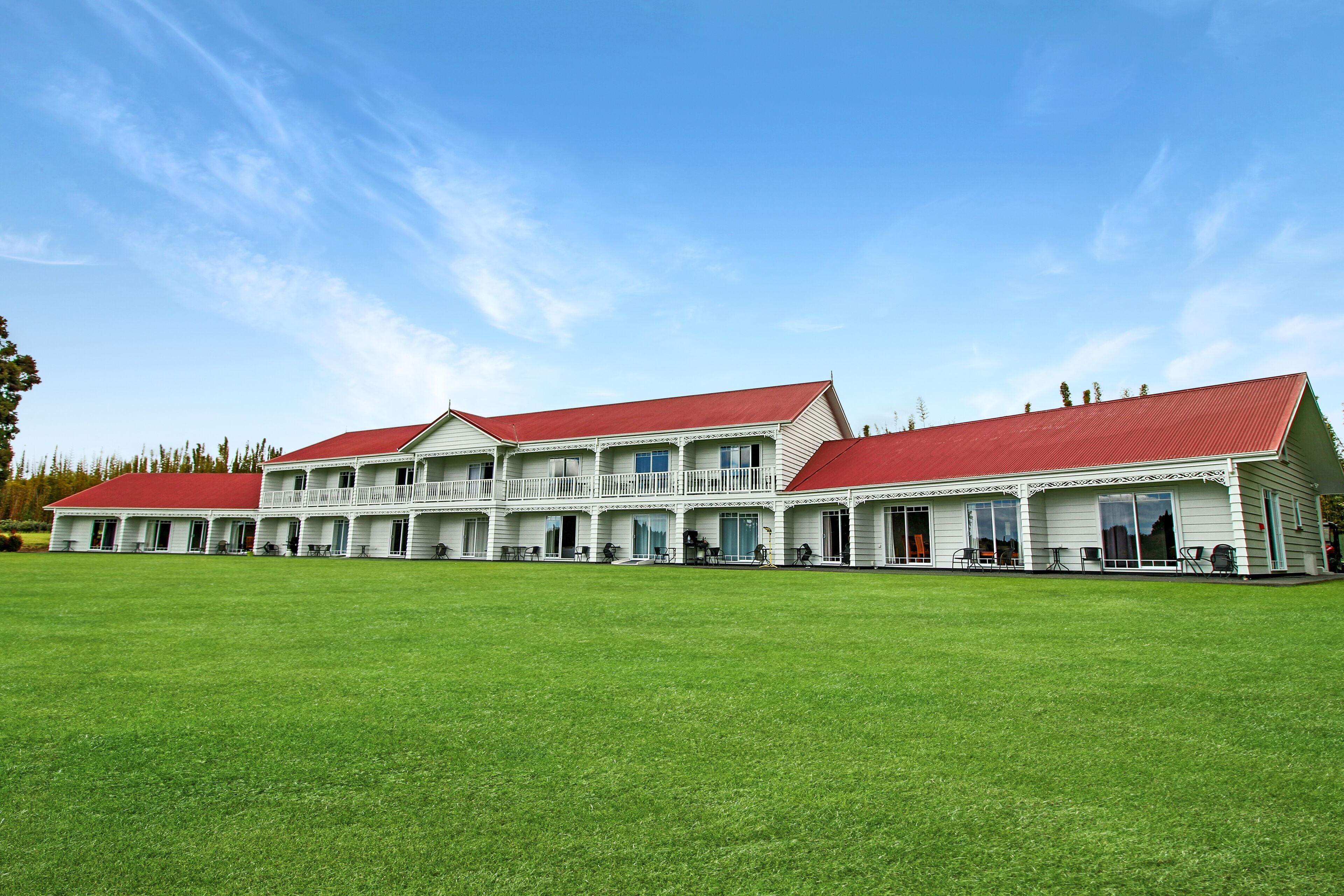 A large, white building with red roofs and multiple balconies, surrounded by a well-maintained lawn.