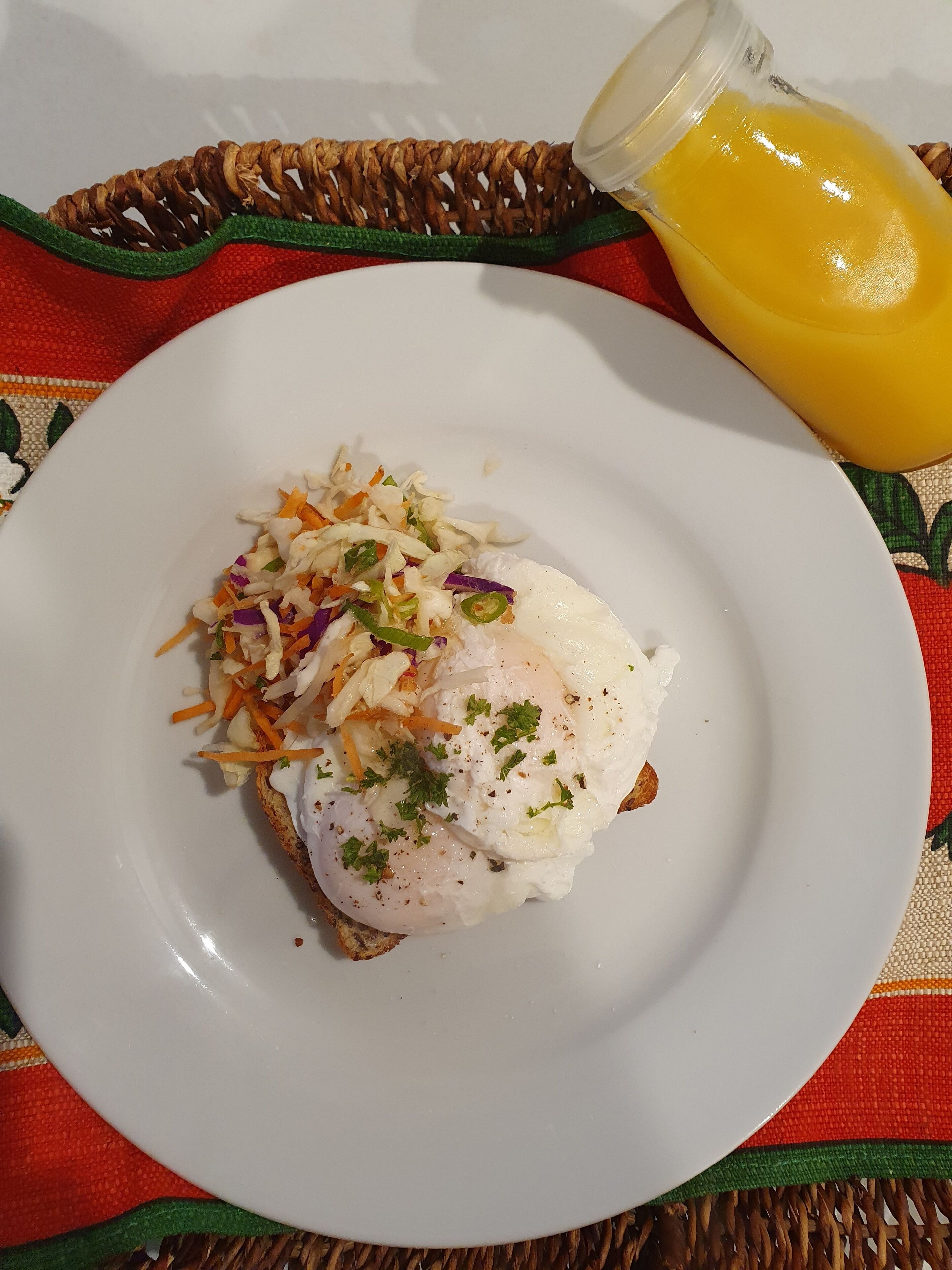 A plate with a poached egg, shredded vegetables, and a glass of orange juice on a table with a woven placemat.