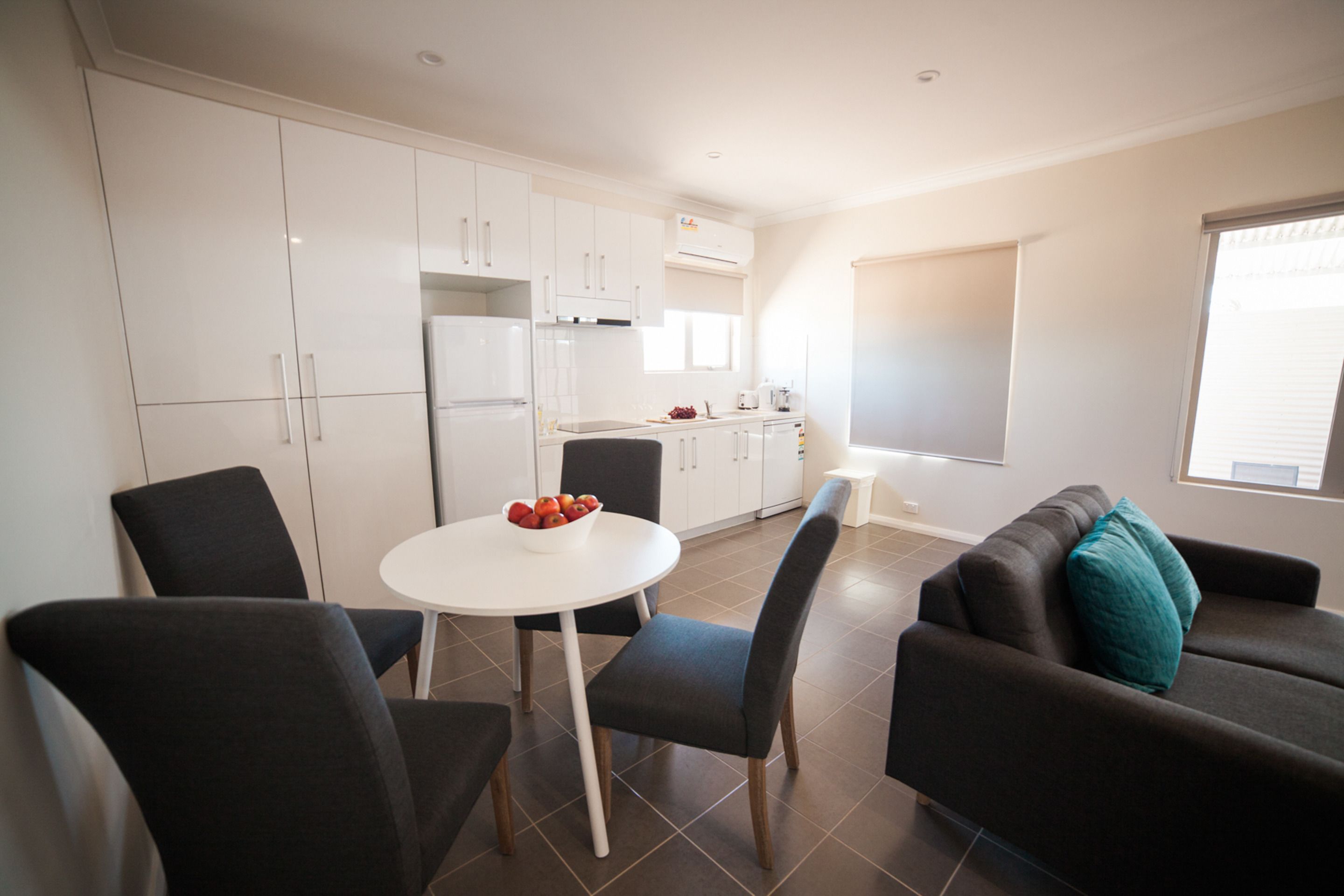 Een moderne keuken met witte kastjes, een eettafel met stoelen en een bank met een blauwgroen kussen.