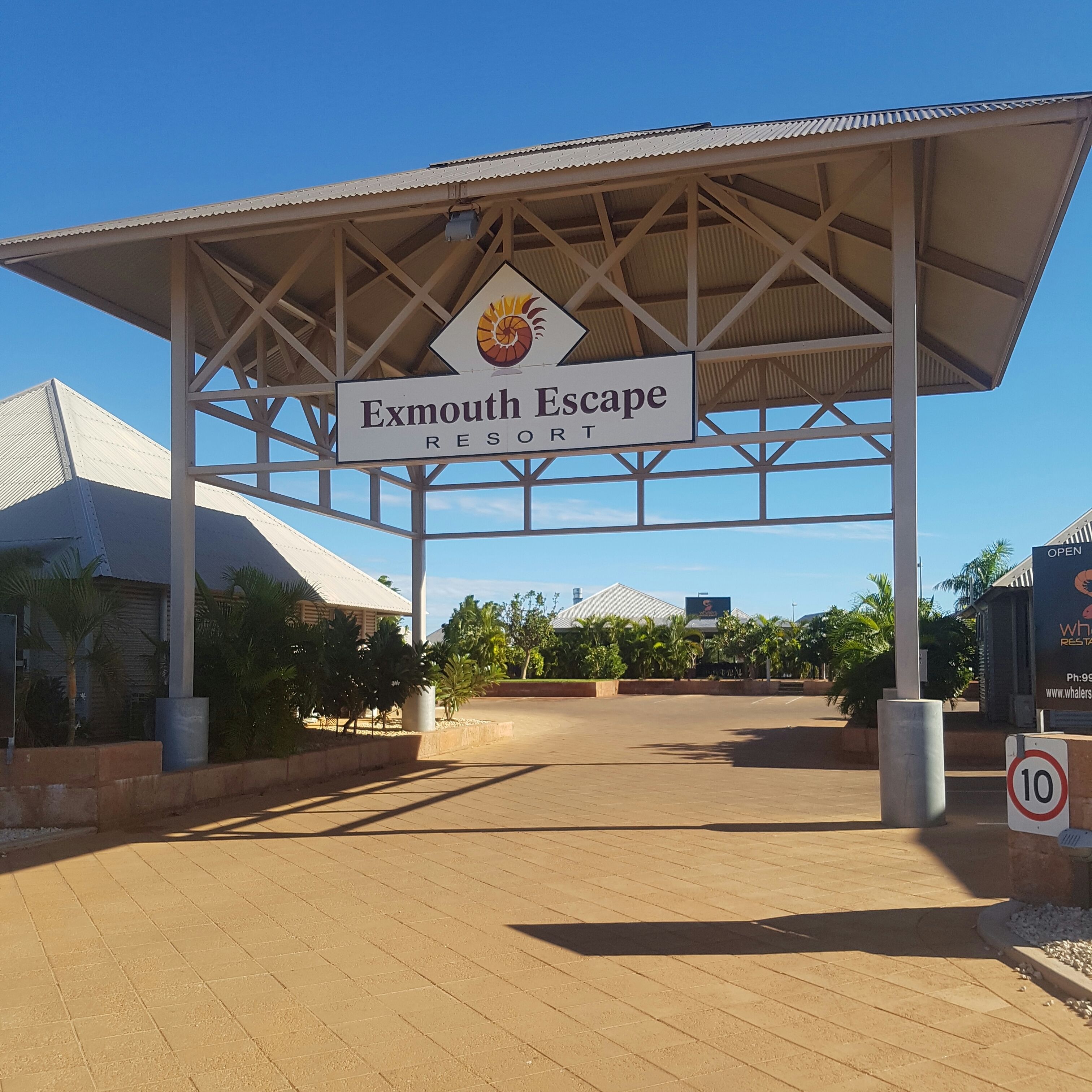 La entrada al Exmouth Escape Resort, con cielo despejado, un letrero y una señal de límite de velocidad.