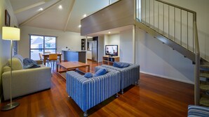 A spacious living area with a high ceiling, a dining table, a sofa, and a staircase. - Exmouth Escape Resort (Exmouth)