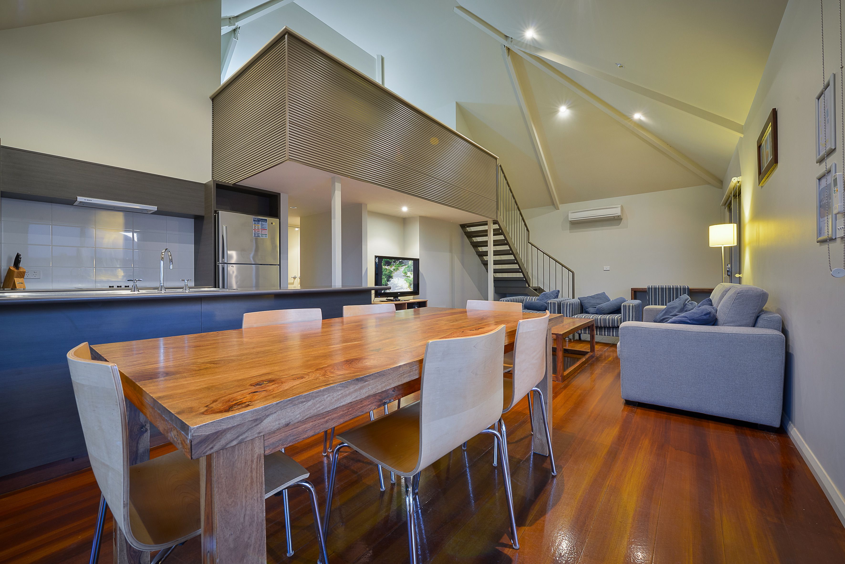 A modern kitchen with a wooden dining table and chairs, a built-in refrigerator, and a TV.