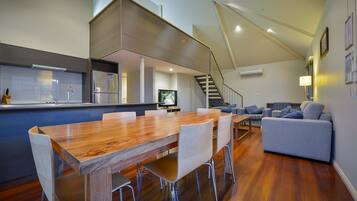 A modern kitchen with a wooden dining table and chairs, a built-in refrigerator, and a TV.