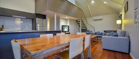 A modern kitchen with a wooden dining table and chairs, a built-in refrigerator, and a TV.