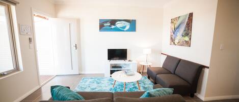 A living room with a sofa, a coffee table, a TV, and artwork on the walls.