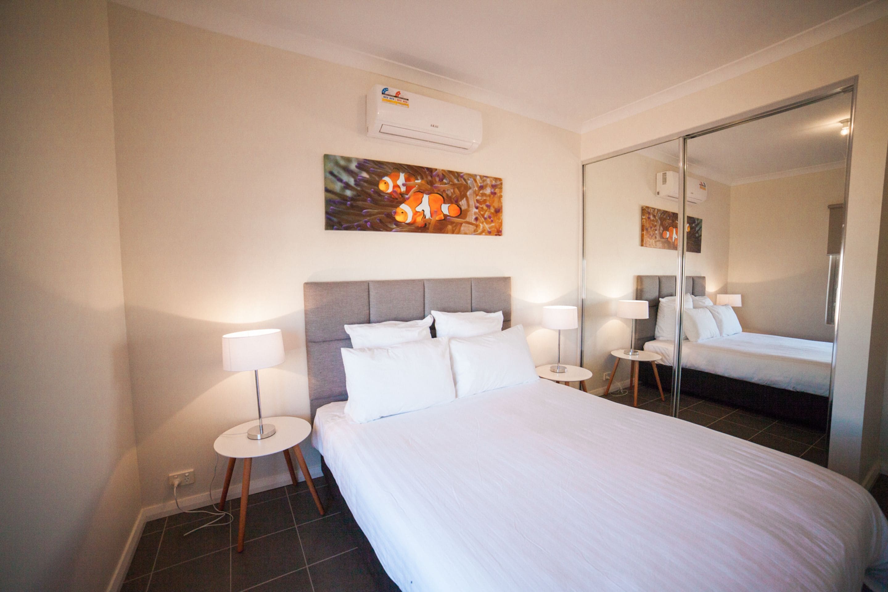 Hotelkamer met een groot bed, twee nachtkastjes met lampen, een hoofdbord, een wandairconditioner en een spiegel.