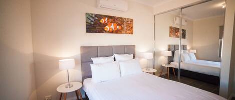 Hotelkamer met een groot bed, twee nachtkastjes met lampen, een hoofdbord, een wandairconditioner en een spiegel.