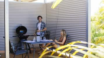An outdoor patio with a grill, a table with chairs, and a person standing by the grill.