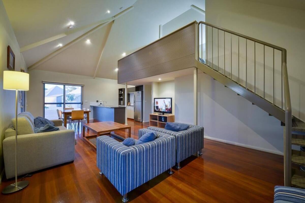 Amplia sala de estar con techo alto, mesa de comedor, sofá, televisor y escalera.
