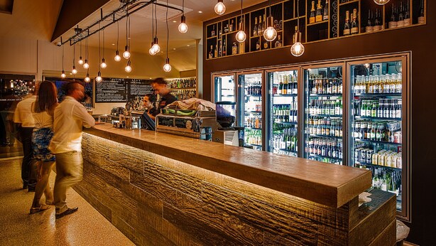 A bar area with a wooden counter, hanging light fixtures, and shelves stocked with bottles. - Exmouth Escape Resort (Exmouth)