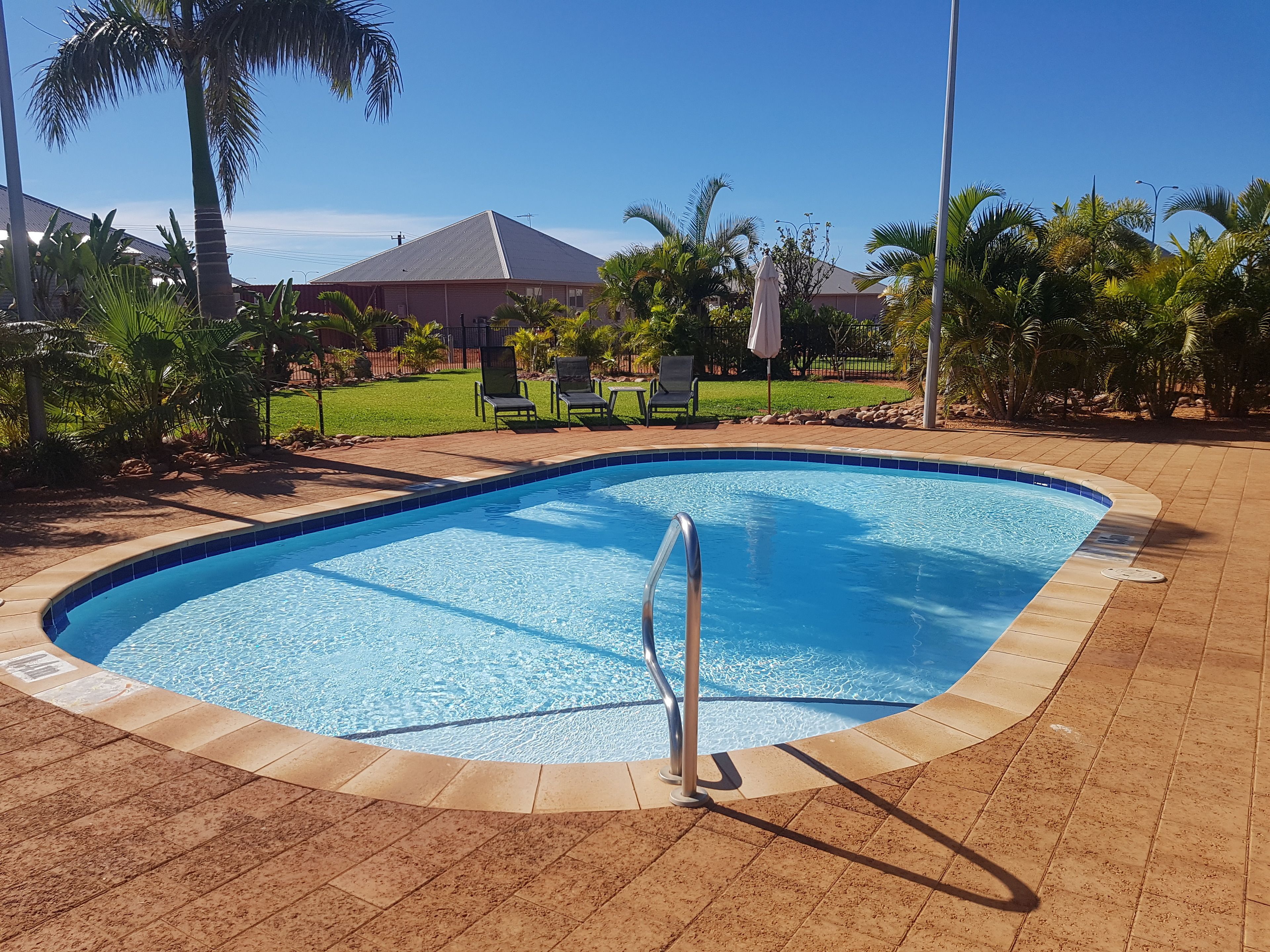 A rectangular swimming pool with a metal ladder, surrounded by a tiled deck.