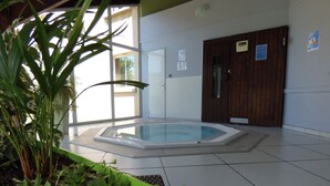 A swimming pool area with a tiled floor, a wooden door, and a green planter with plants. - Brit Hotel Confort Villefranche de Rouergue (Villefranche-de-Rouergue)
