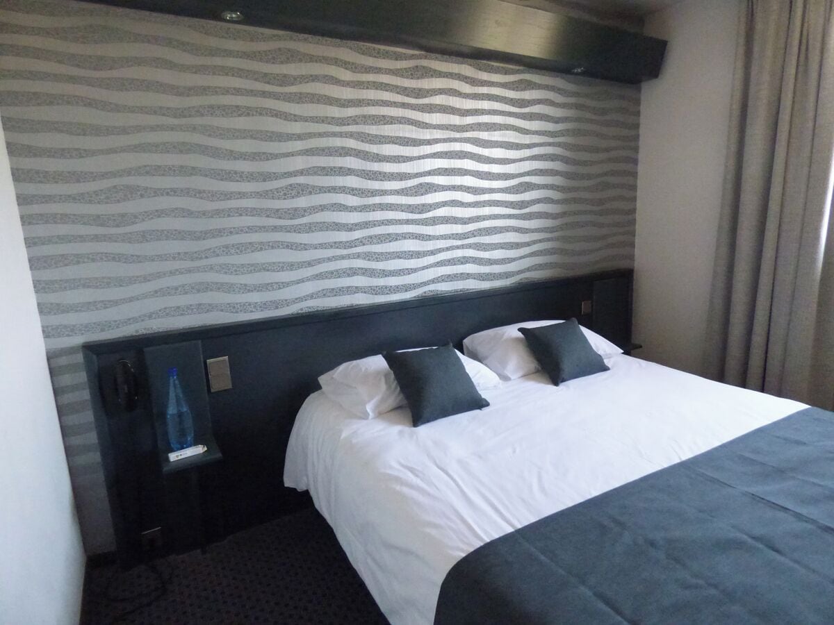 A hotel room with a bed, a nightstand, a water bottle, and a patterned wall.