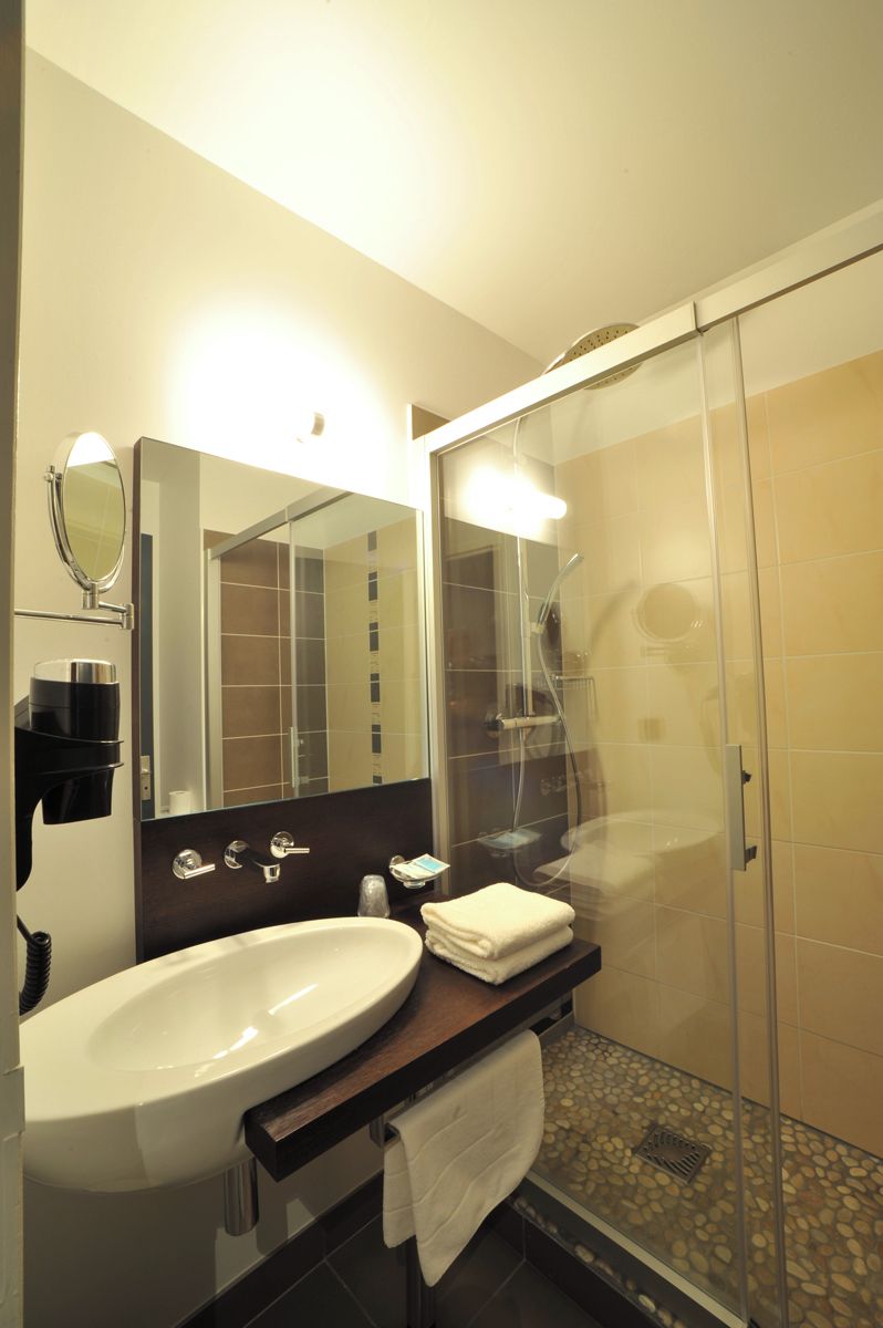 A modern bathroom with a large sink, a mirror, a glass shower enclosure, and a towel rack.