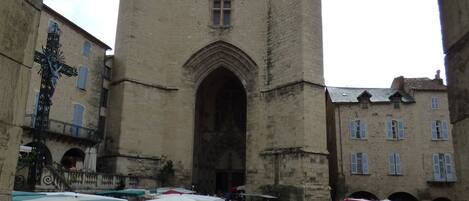 A medieval building with a large arched entrance, surrounded by market stalls with umbrellas.